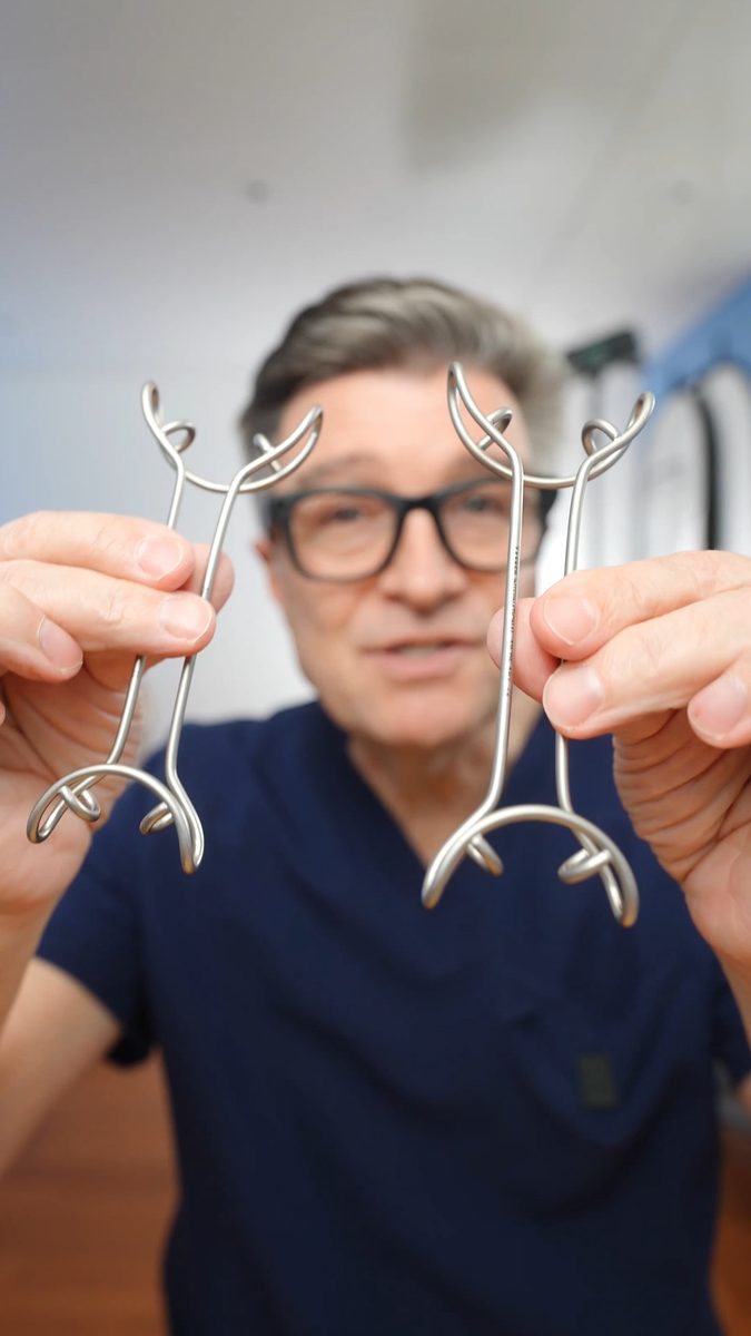 Dr. Alessandro Devigus holding a pair of his stainless steel cheek retractors